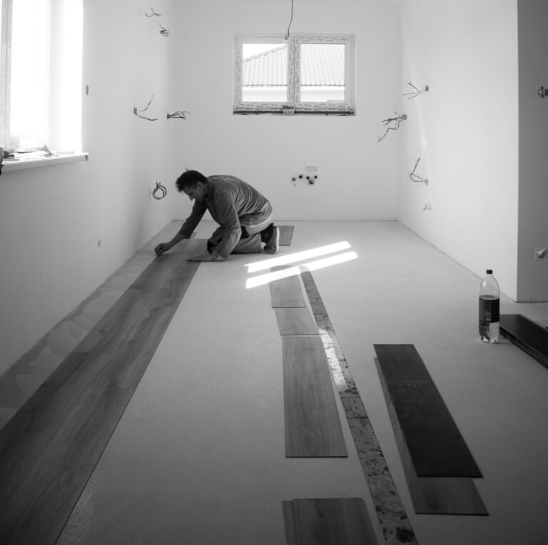 Man installing vinyl plank flooring in a partially finished duplex room